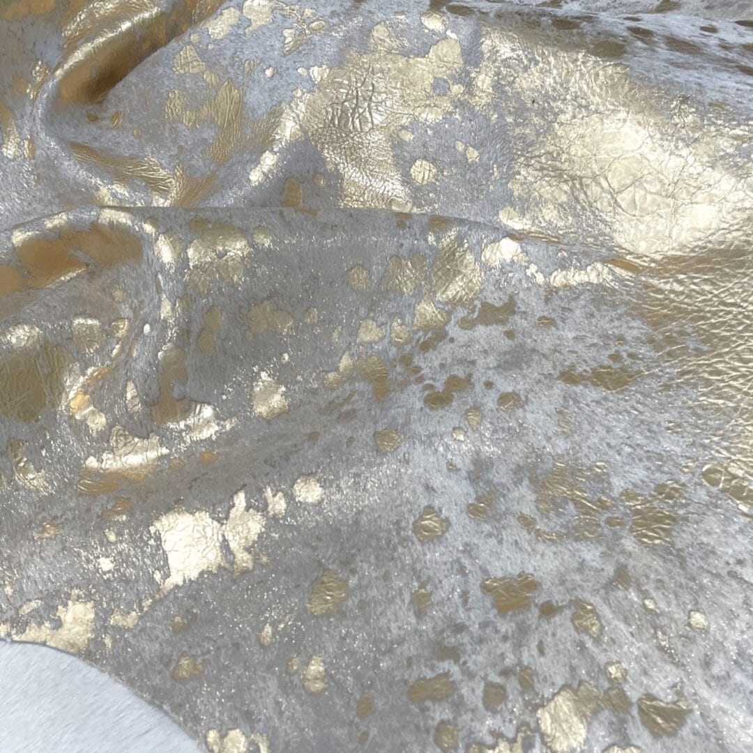 Devore-Gold This stunning hair-on cowhide features a luxurious metallic gold overlay on a natural white base, creating a perfect balance of glam and organic beauty. Ideal for handbags, upholstery, wall art, footwear, and fashion accessories.