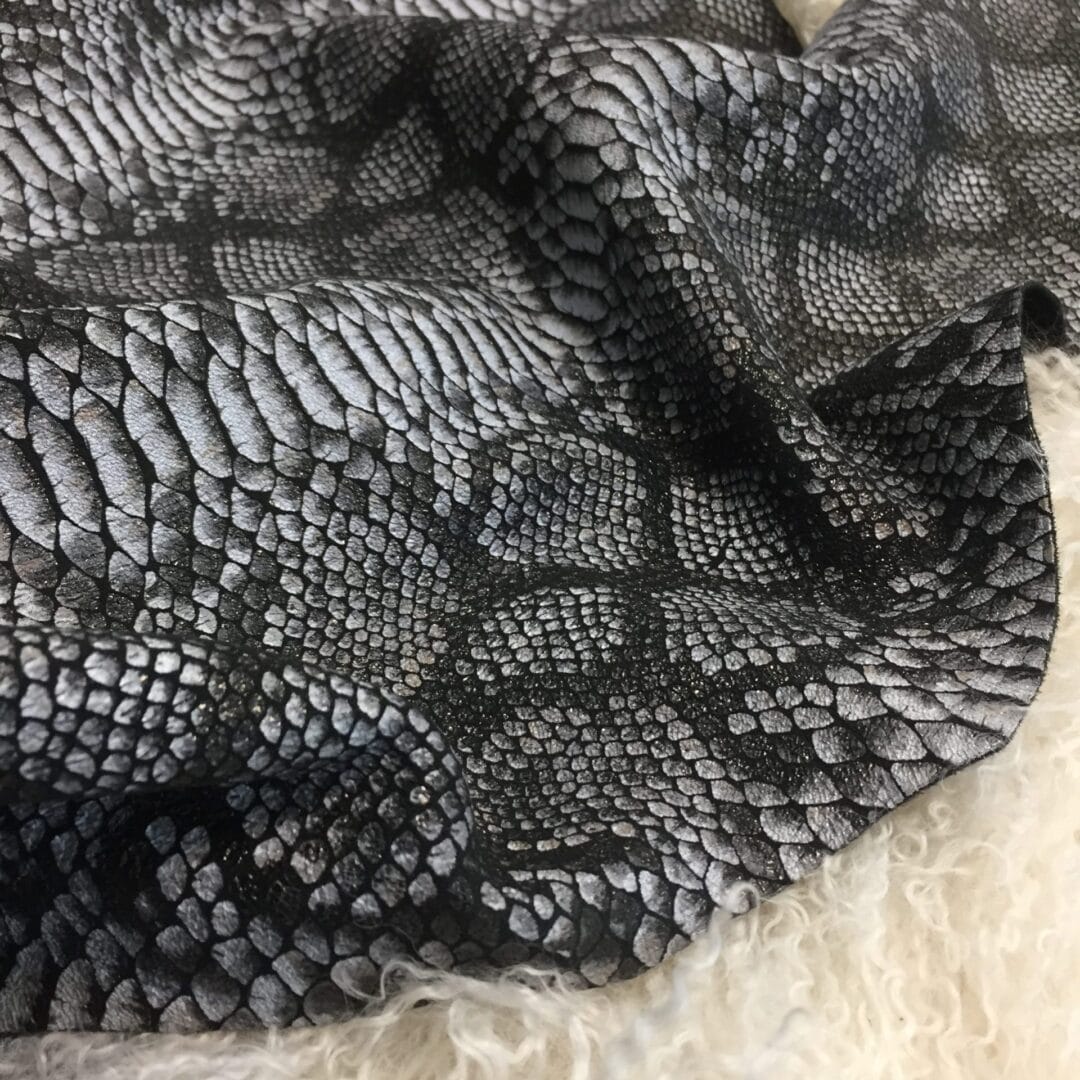 Rizzy Snake Lambskin avetcoinc@ (5) This Lambskin leather is a stunning hide printed with a captivating snakeskin pattern, featuring an alluring combination of exotic colors that sets it apart from other leathers. The leather has a slightly textured surface with a bit of stretch, making it highly versatile for various projects. This leather has a unique yet sophisticated appearance that complements modern fashion trends, making it a highly sought-after item in the fashion industry. It is highly versatile and perfect for creating a range of products such as apparel, wallets, accessories, handbags, shoes, and more. Its unique texture, pattern, and color combination make it an ideal choice for designers looking to create high-quality, fashionable products. This leather is made from high-quality Lambskin and features a unique snake print pattern that is highly desirable in the fashion industry. The leather is tanned using the Chrome tanning process, which gives it a unique texture and added durability. The average hide size is 7 square feet, making it perfect for creating a range of products, and the leather thickness ranges from 0.7 to 0.9 mm, giving it a soft and supple feel. The leather is sourced from Turkey, which is known for producing high-quality leathers that are sought after by designers around the world.