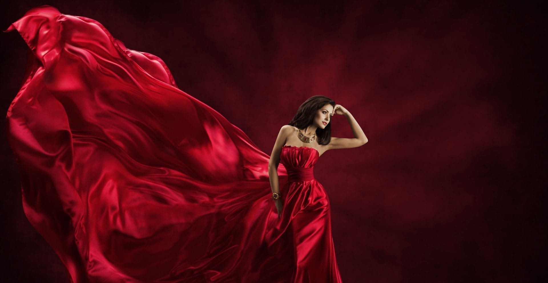 High fashion model in luxurious red gown emphasizing accessories and flowing fabric