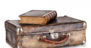 "Old leather-bound book atop antique suitcase symbolizing timeless fashion and accessories."