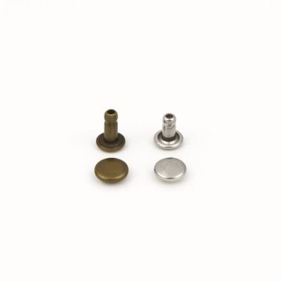 Four double cap rivets in nickel and antique brass finishes, neatly arranged on a white background for size comparison.