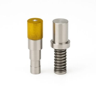 Two cylindrical metal die setters with a spring and yellow top insert, displayed upright on a clean white background.