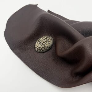Antique floral concho button displayed on textured brown leather surface