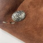 Backside of an antique floral concho button inserted into suede leather showing double prong placement