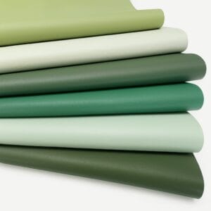 Stacked pieces of smooth full-grain cow leather in green tones, arranged on a white background, part of the Milano Collection by Avetco.