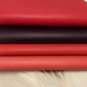 Four stacked layers of smooth Milano cowhide leather in rich red, burgundy, coral, and rose tones, displayed on a light fur background. Article features a subtle natural grain and soft texture, ideal for accessories and leather goods.-Avetco