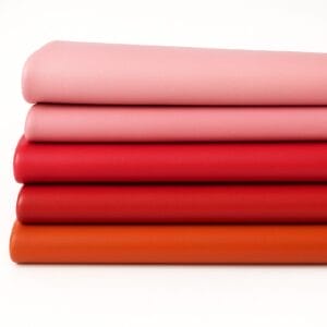 Five rolls of Milano Collection smooth cowhide leather in red, orange, and pink tones, featuring natural grain and soft handfeel, laid on a white background.