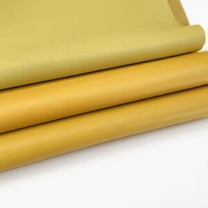 Stacked pieces of smooth full-grain cow leather in yellow tones, arranged on a white background, part of the Milano Collection by Avetco.