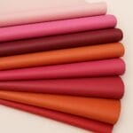 SL-101 Reds Oragesand Pinks Lambskin 8-10 sq ft | Avetco Leather Hides and Eva Foam Stacked lambskin leather rolls in red, pink, coral, blush, and orange tones on a white background.-Avetco