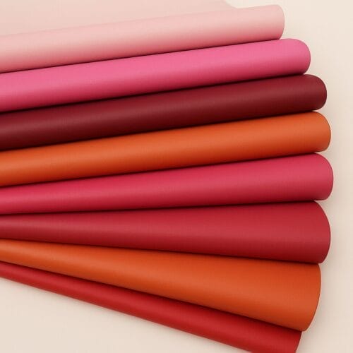 Stacked lambskin leather rolls in red, pink, coral, blush, and orange tones on a white background.-Avetco