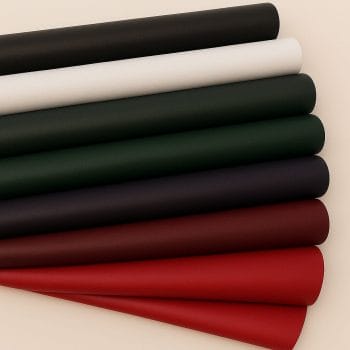 Seven lambskin leather rolls in black, white, polo green, purple, deep red, and red colors, neatly stacked against a soft off-white background.-Avetco