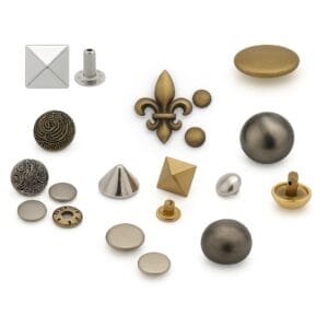 "Collage of assorted decorative metal rivets and studs on a clean white background, including pyramid, dome, cone, fleur-de-lis, and flat round styles.